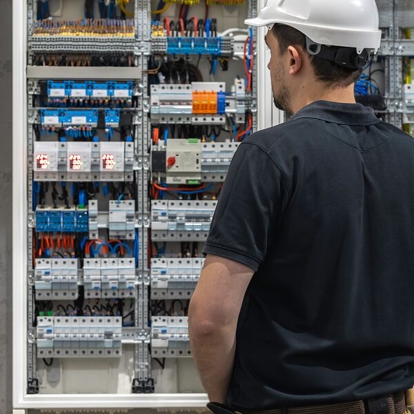 Un électricien qualifié portant des gants de protection en train d'installer ou de vérifier des disjoncteurs dans un panneau électrique de 200 ampères.
