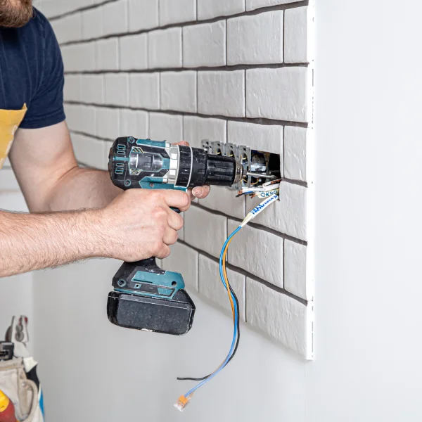 Un homme utilise une perceuse pour installer une prise murale dans une maison.