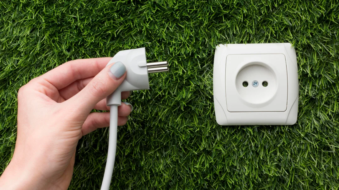 Une main tient une prise électrique sur l'herbe, illustrant l'installation de prise électrique.