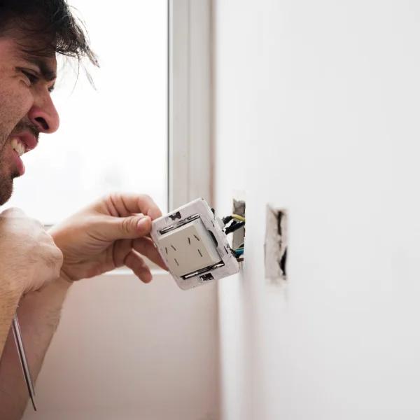 Un homme répare un interrupteur électrique dans un environnement domestique.