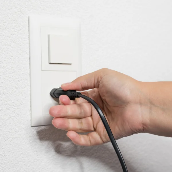Une personne tient un cordon noir près d'une prise électrique.