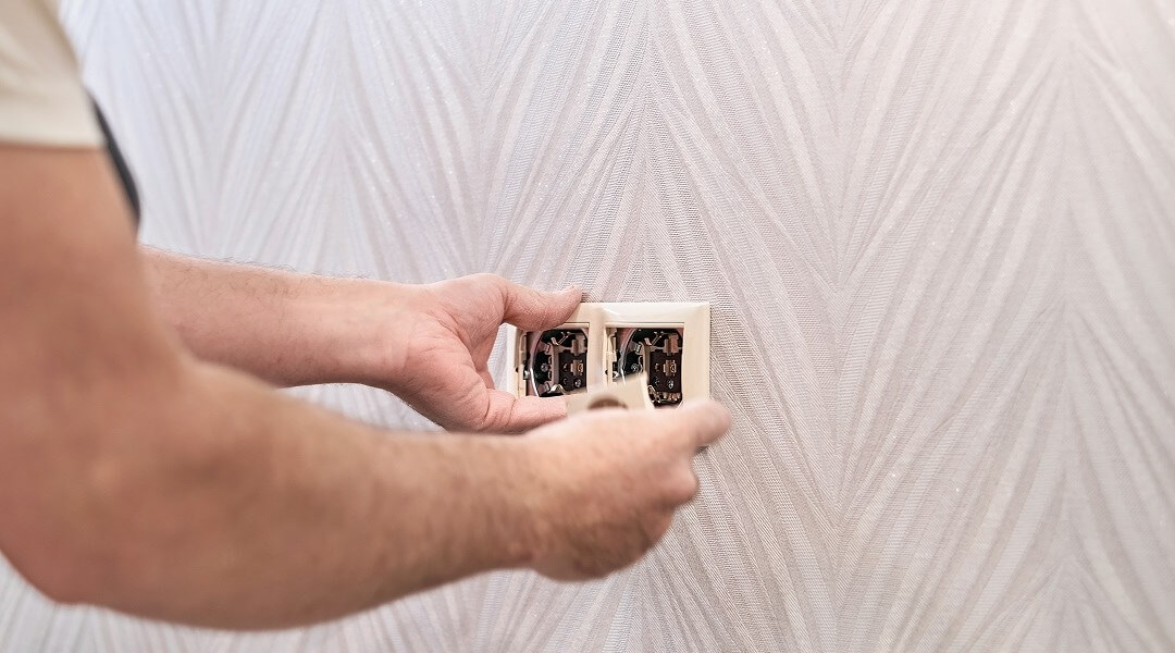 Électricien installant une plaque de finition sur une double prise.